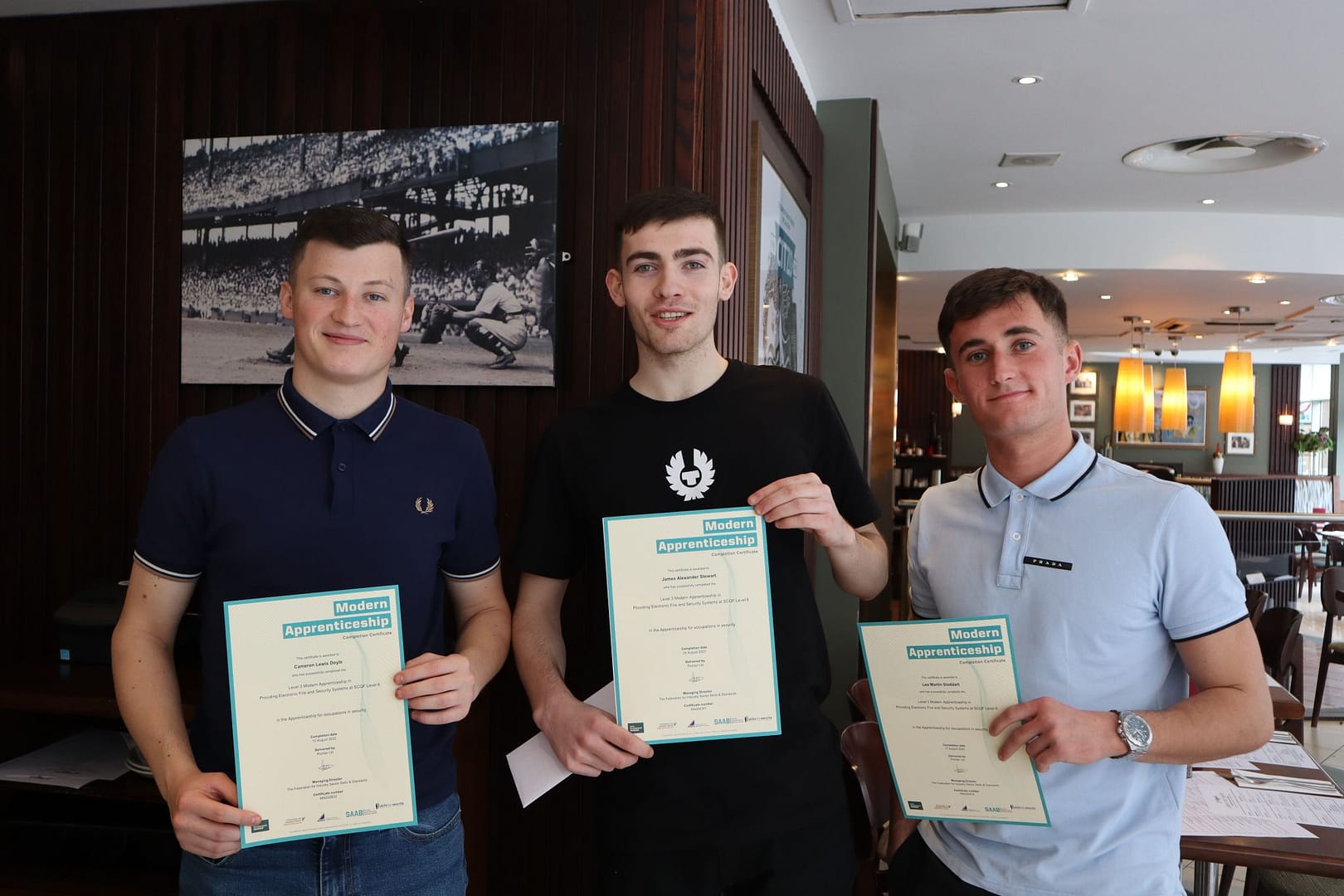 Three apprentices holding certificates in a restaurant setting